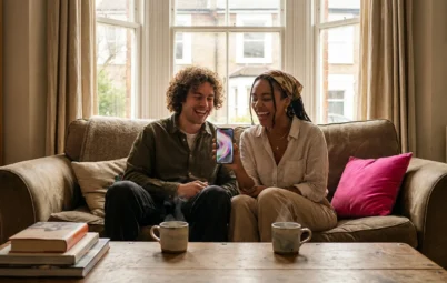 Two friends laughing at a phone on a sofa in a bright living room